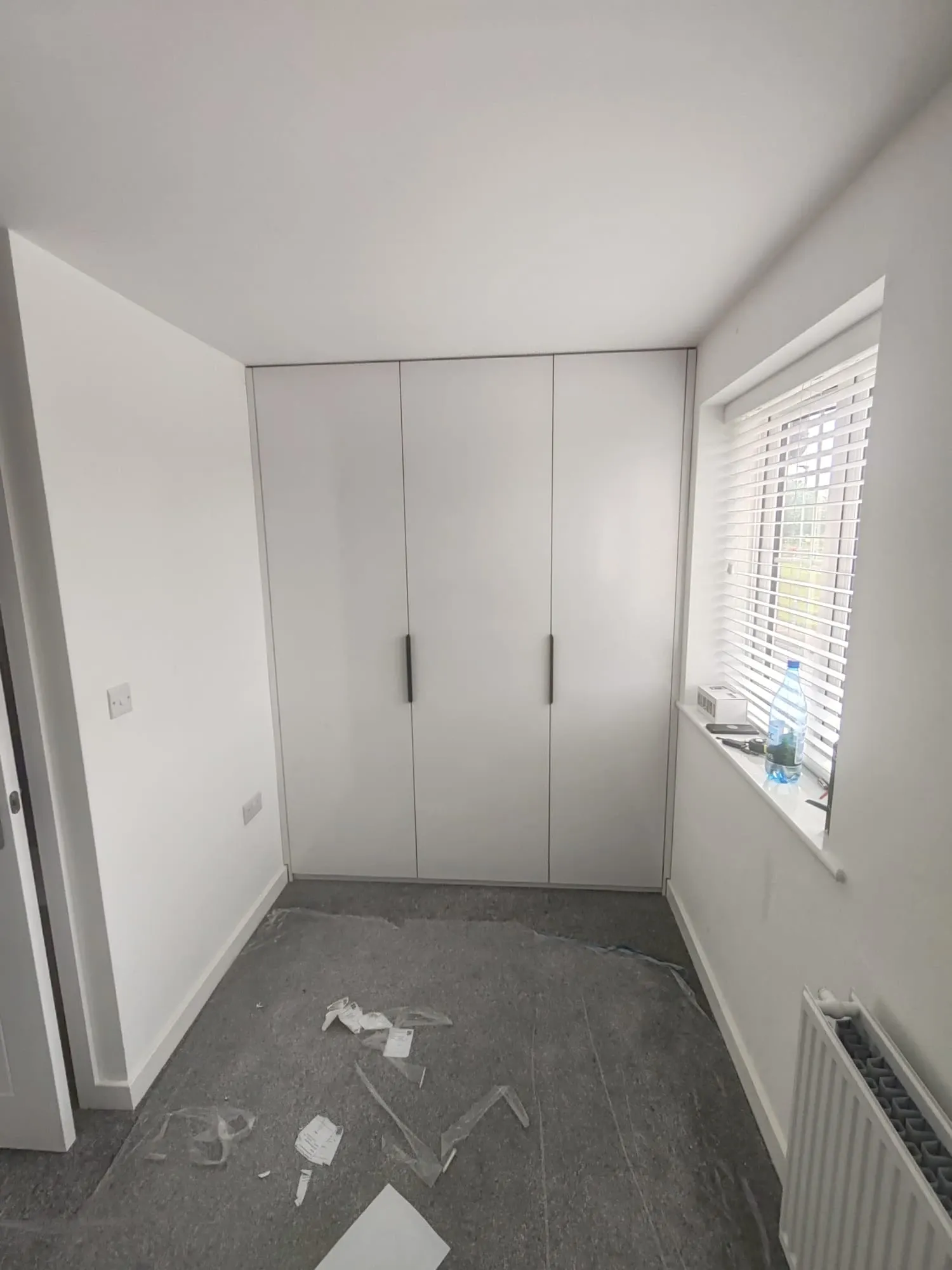 Interior view of a room with custom white cabinets reaching the ceiling and a radiator, offering ample storage and warmth.