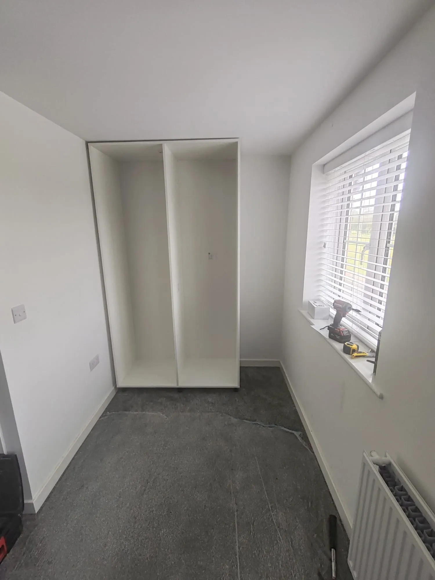 A room featuring a radiator and a partially constructed custom wardrobe in the early stages of assembly.
