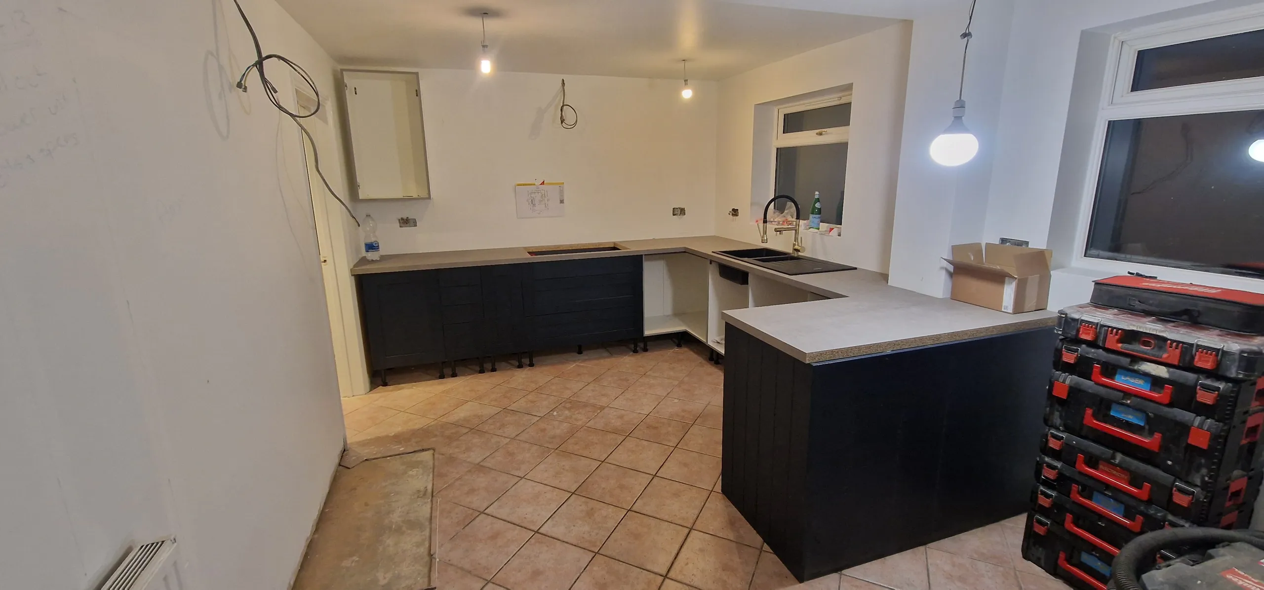 A partially remodelled kitchen featuring a sink and countertop, showcasing construction materials and unfinished areas