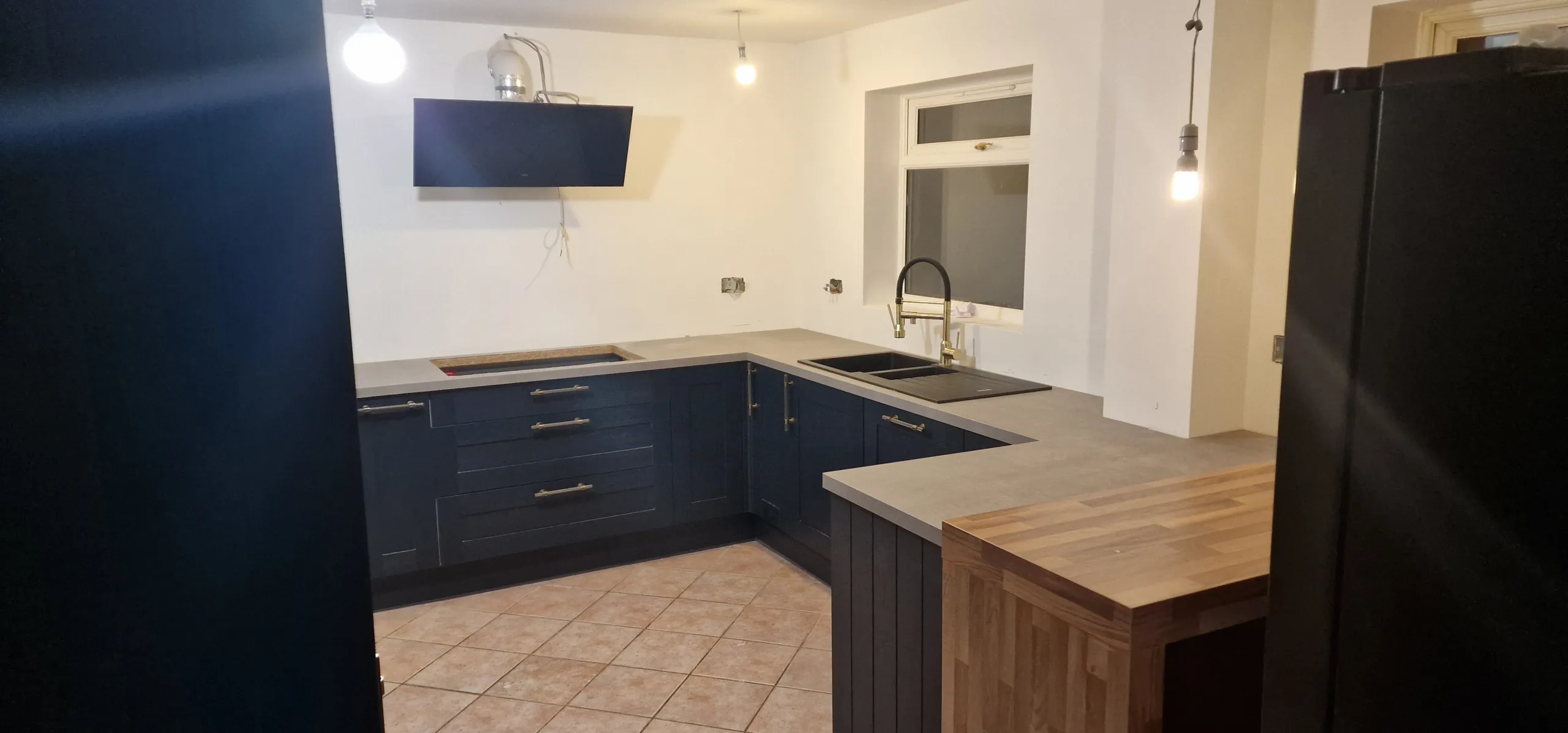 Kitchen remodelling scene showing a sink, countertop, full cupboards, and an extractor fan, highlighting progress in the renovation