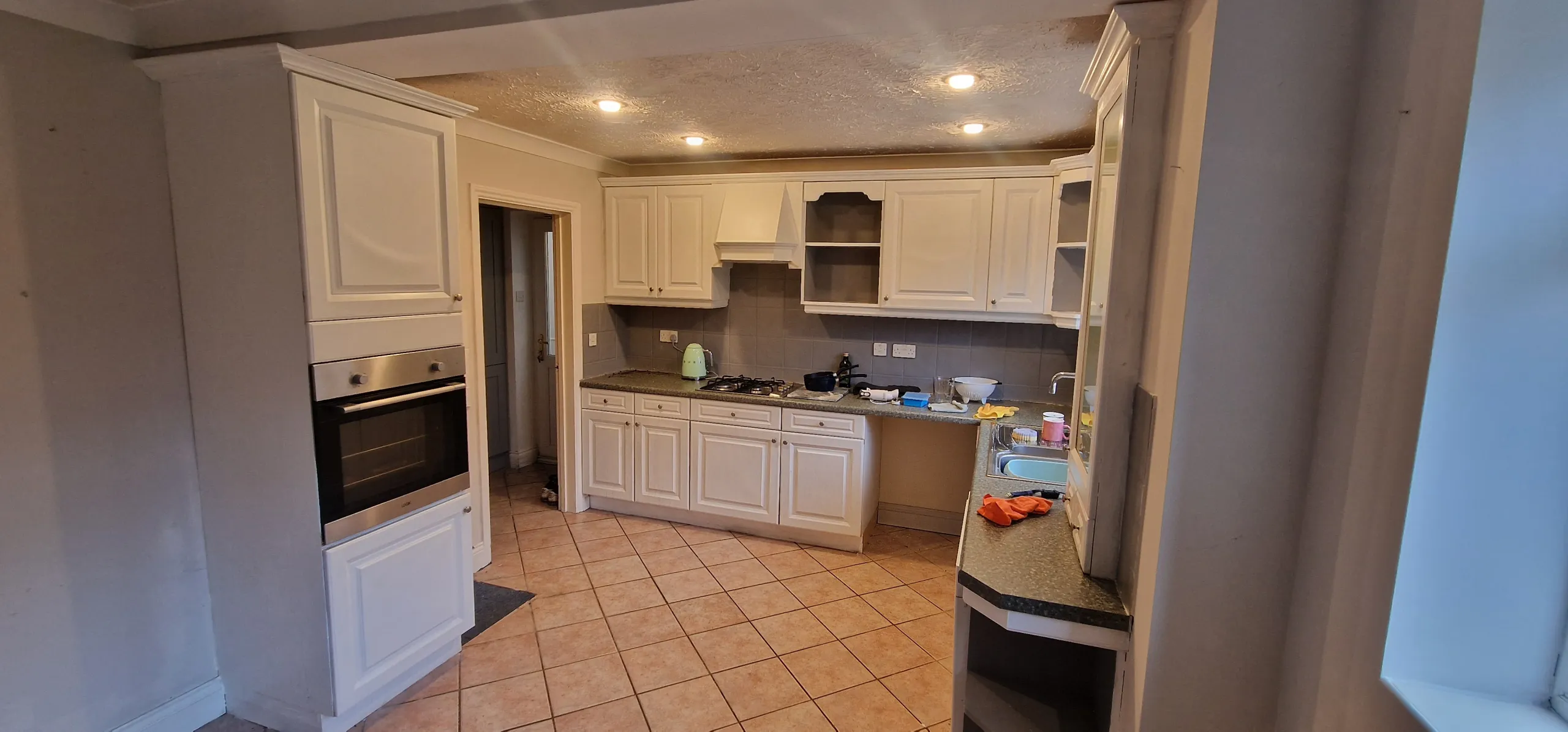 An old-style kitchen with white cabinets and tile flooring, lacking effective space and storage solutions.