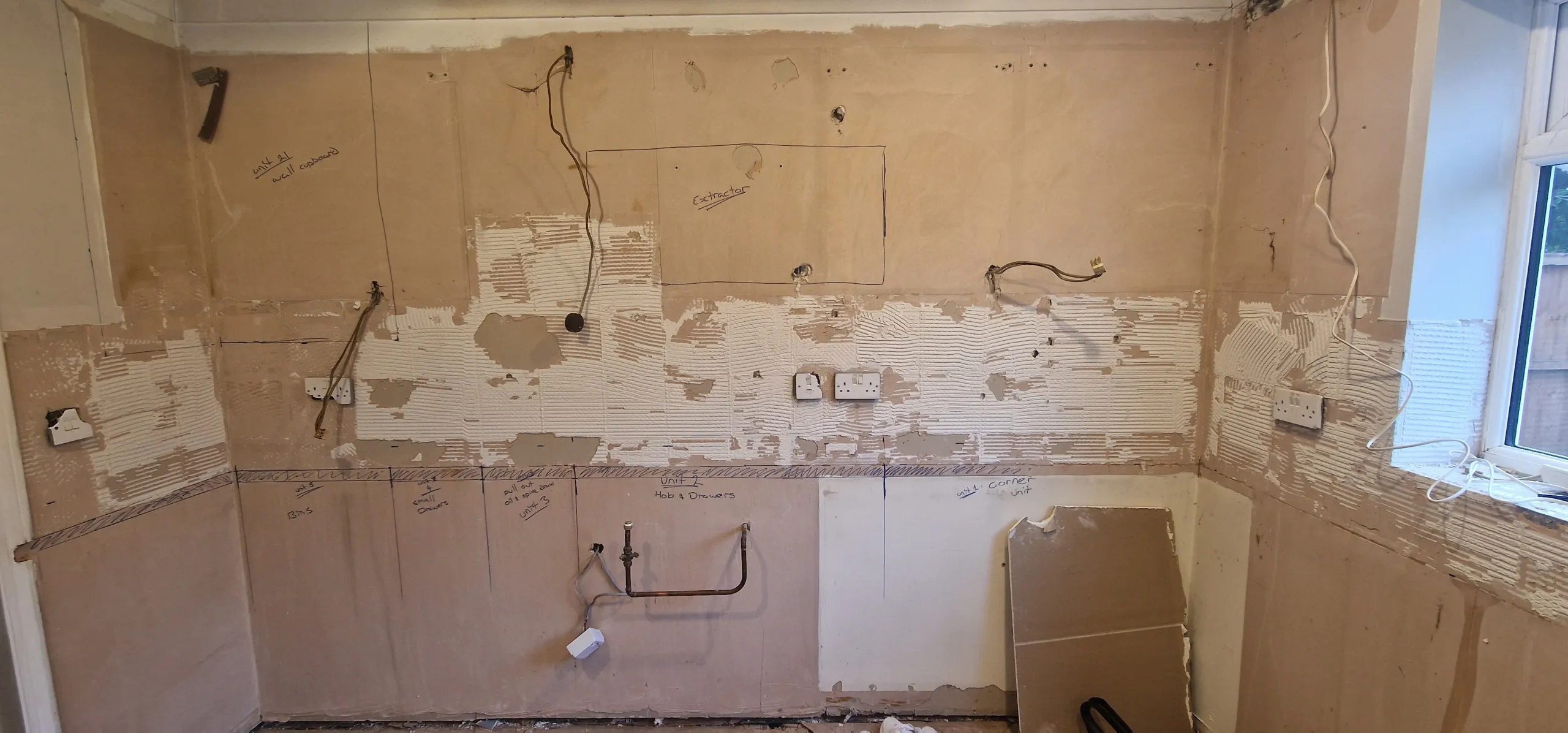 A kitchen with exposed drywall and paint, featuring drawings on the wall for planned kitchen cupboards and appliances.