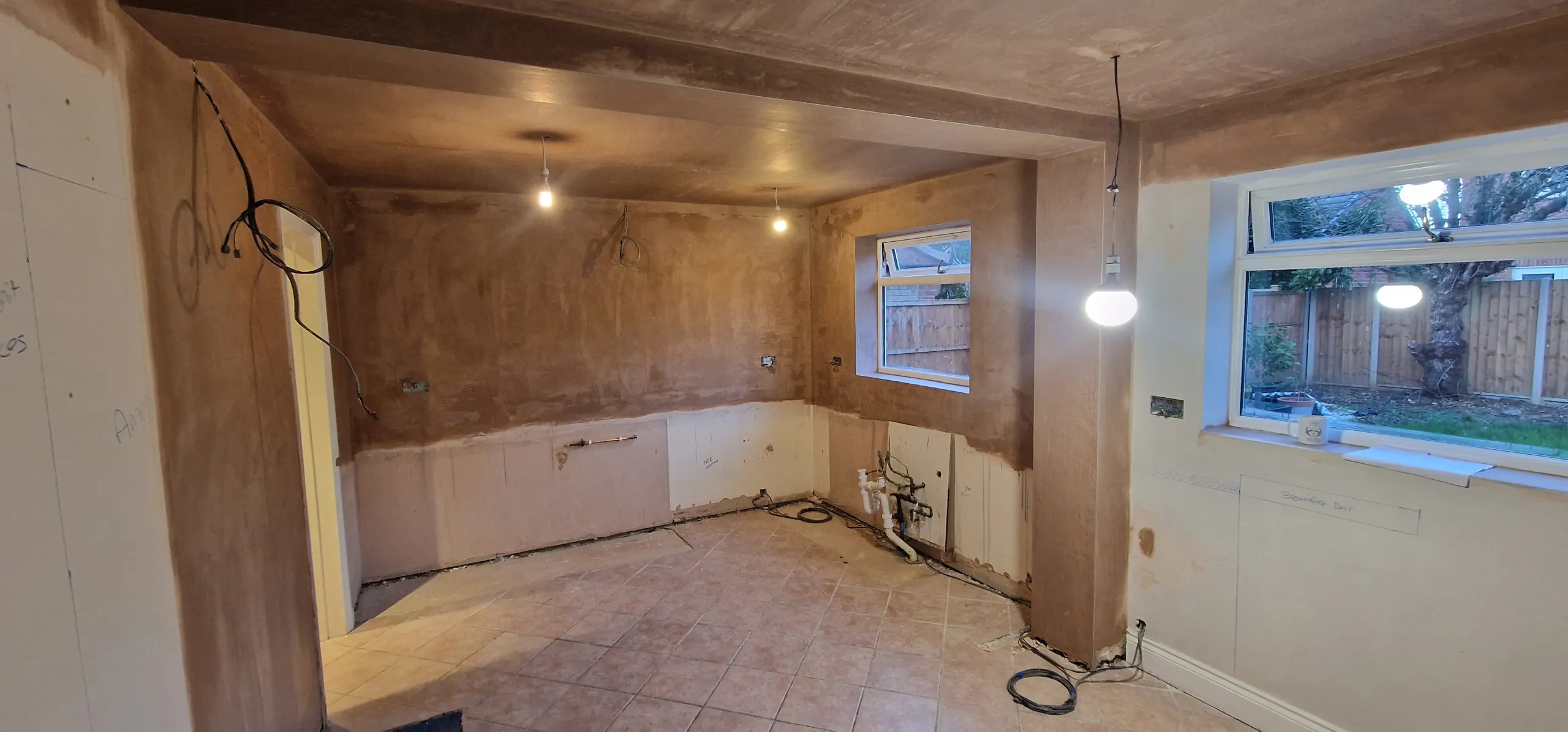 A newly plastered kitchen with a window and a light bulb, highlighting the room's fresh and unfinished look.