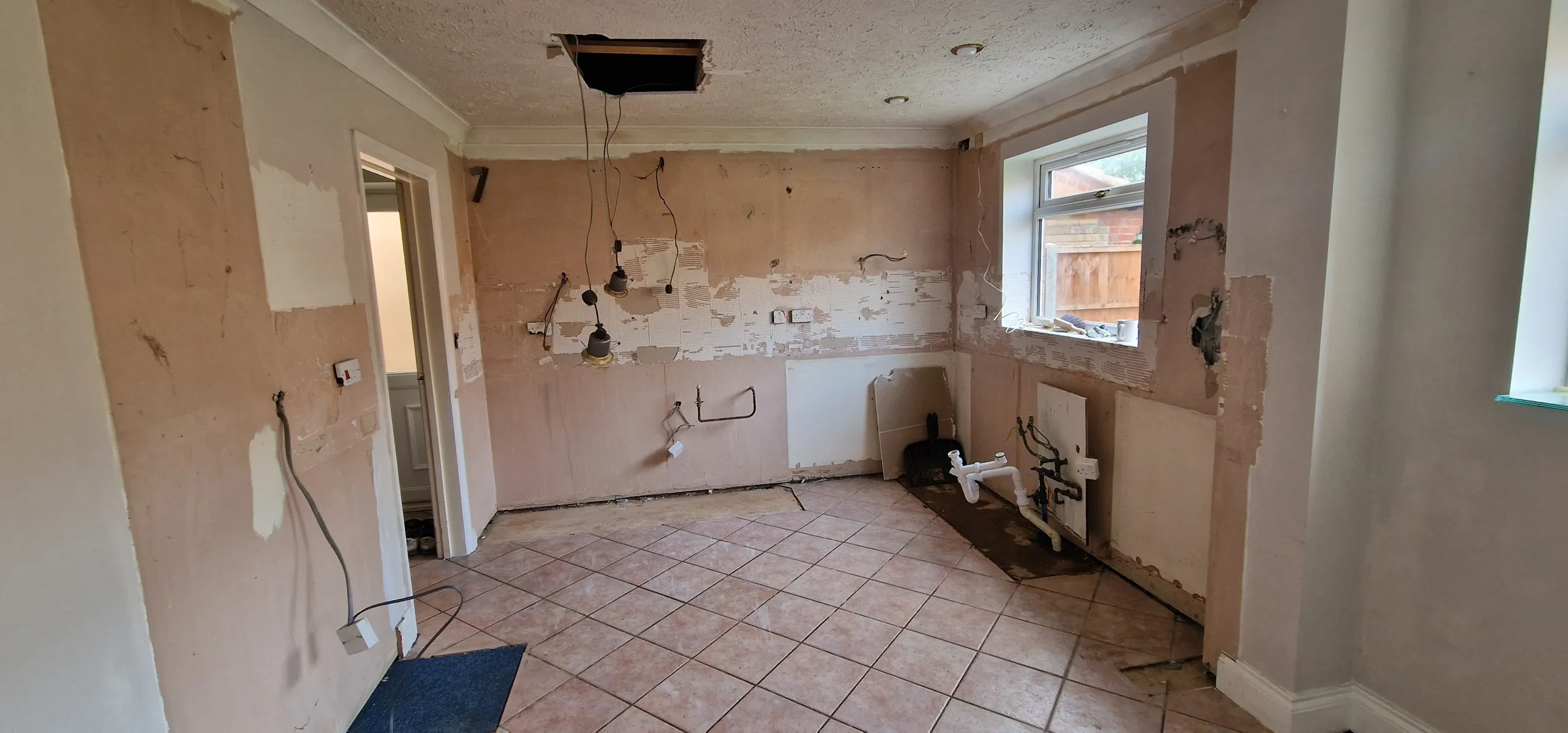 An old-style kitchen with a tiled floor and a window, stripped down and ready for a remodel.