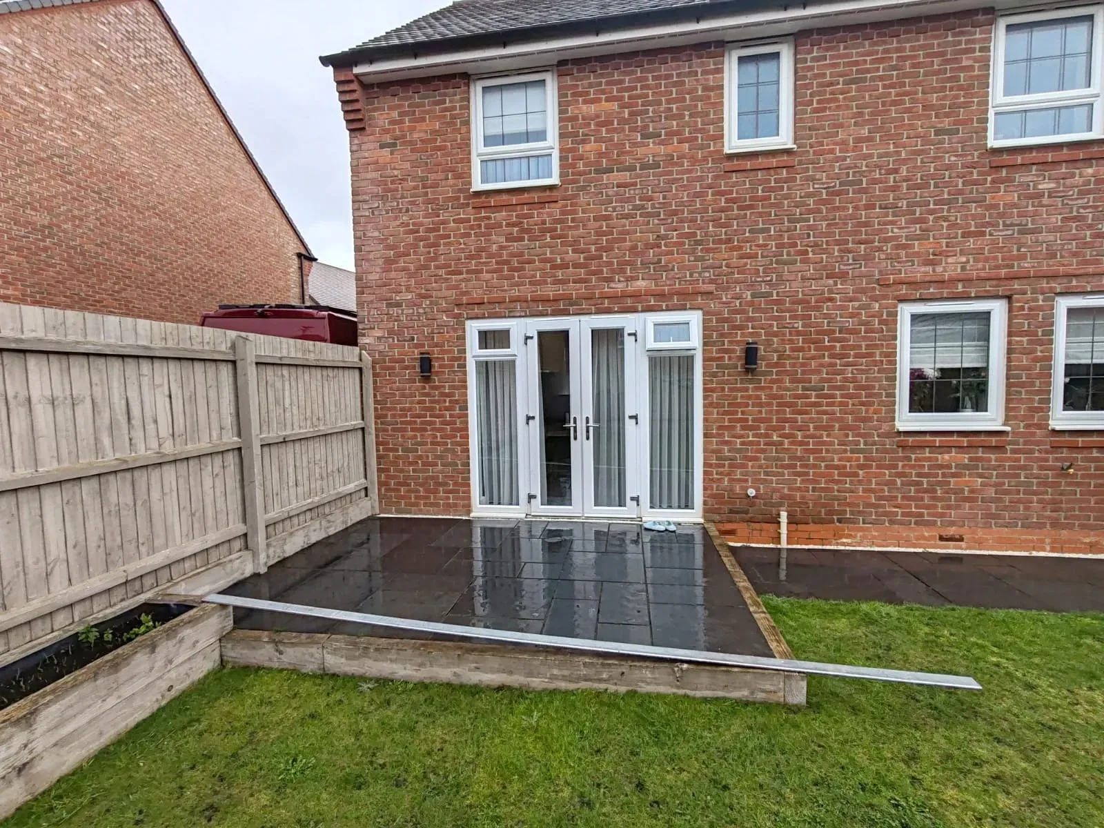 A small patio area featuring a fence and a door, surrounded by unused garden space.
